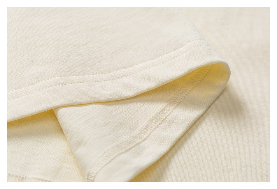 Close-up of a cream garment hem, showing the folded edge and overlock stitching underneath.