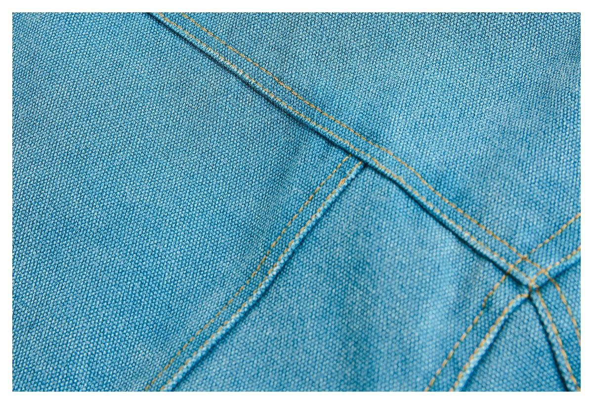 Close-up of blue woven fabric with diagonal seams and contrasting golden-orange stitching.