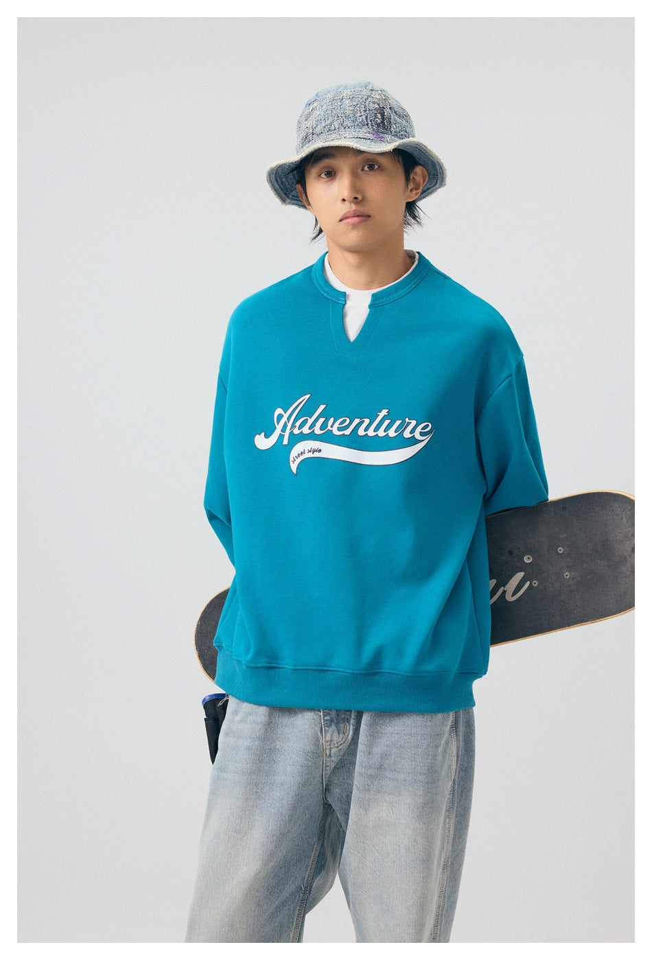 Model wearing a teal sweatshirt with a white script chest graphic, shown from the front.