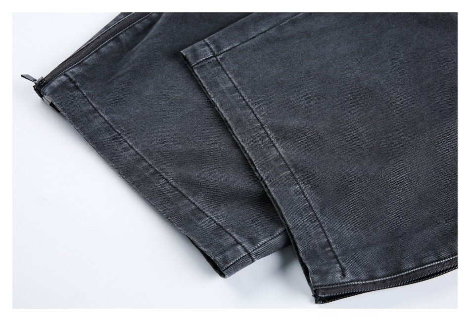 Close-up of overlapping dark charcoal jeans hems, with a small zipper visible at one leg opening.
