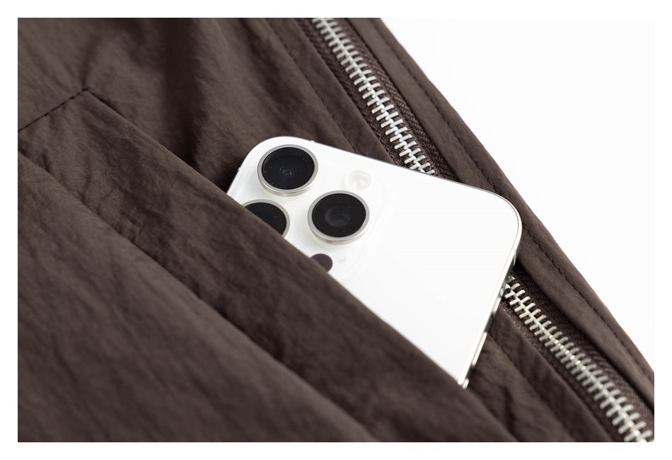White phone tucked into a pocket of a dark brown jacket beside a silver zipper.