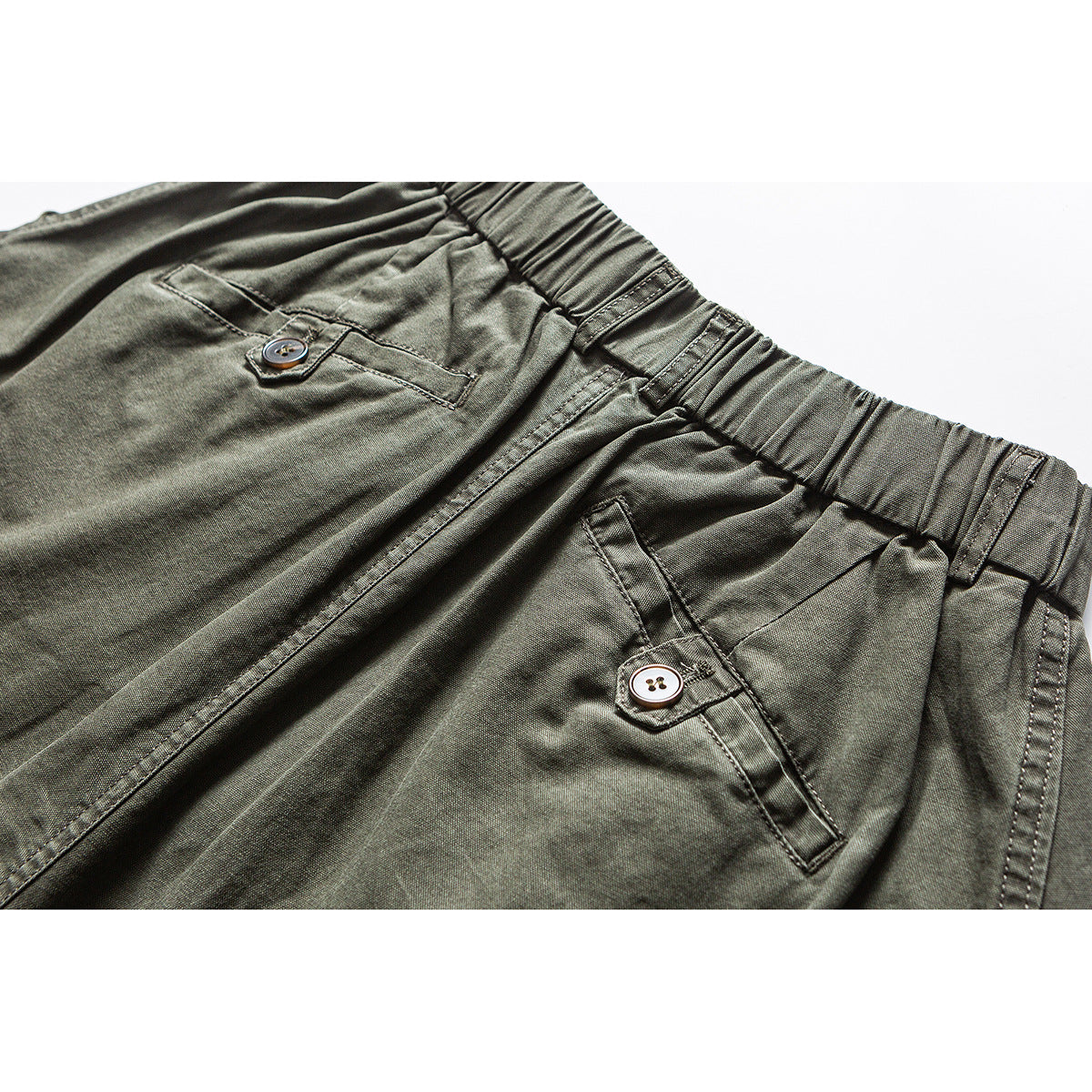 Close-up of olive cargo pants showing the elastic waistband, buttoned pocket flaps, and angled side pockets.