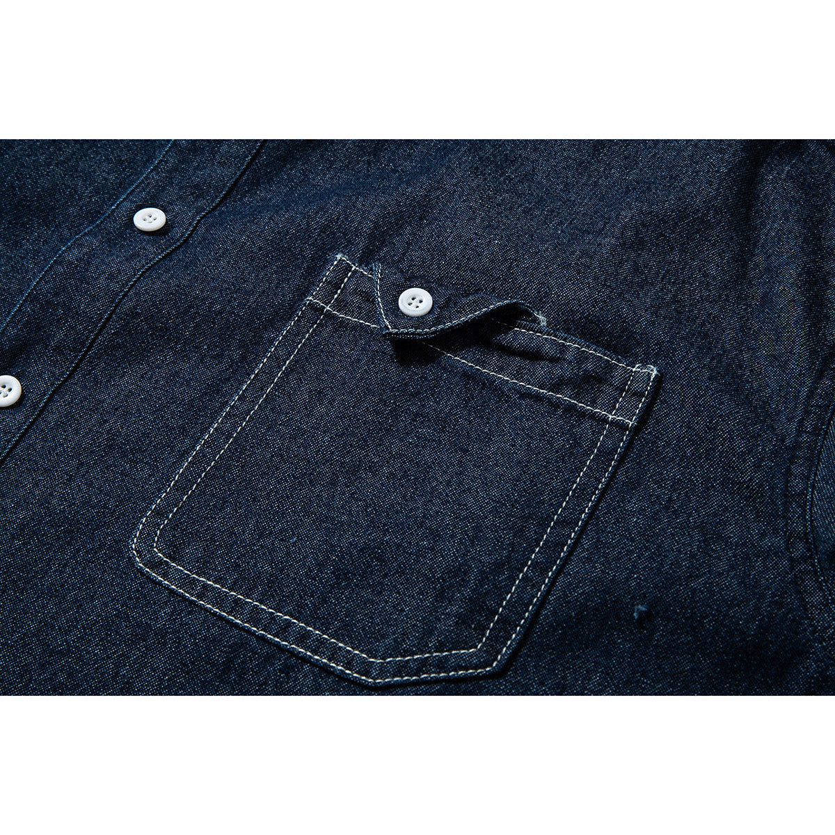 Close-up of a dark indigo shirt's single chest pocket with contrast stitching and a white button.