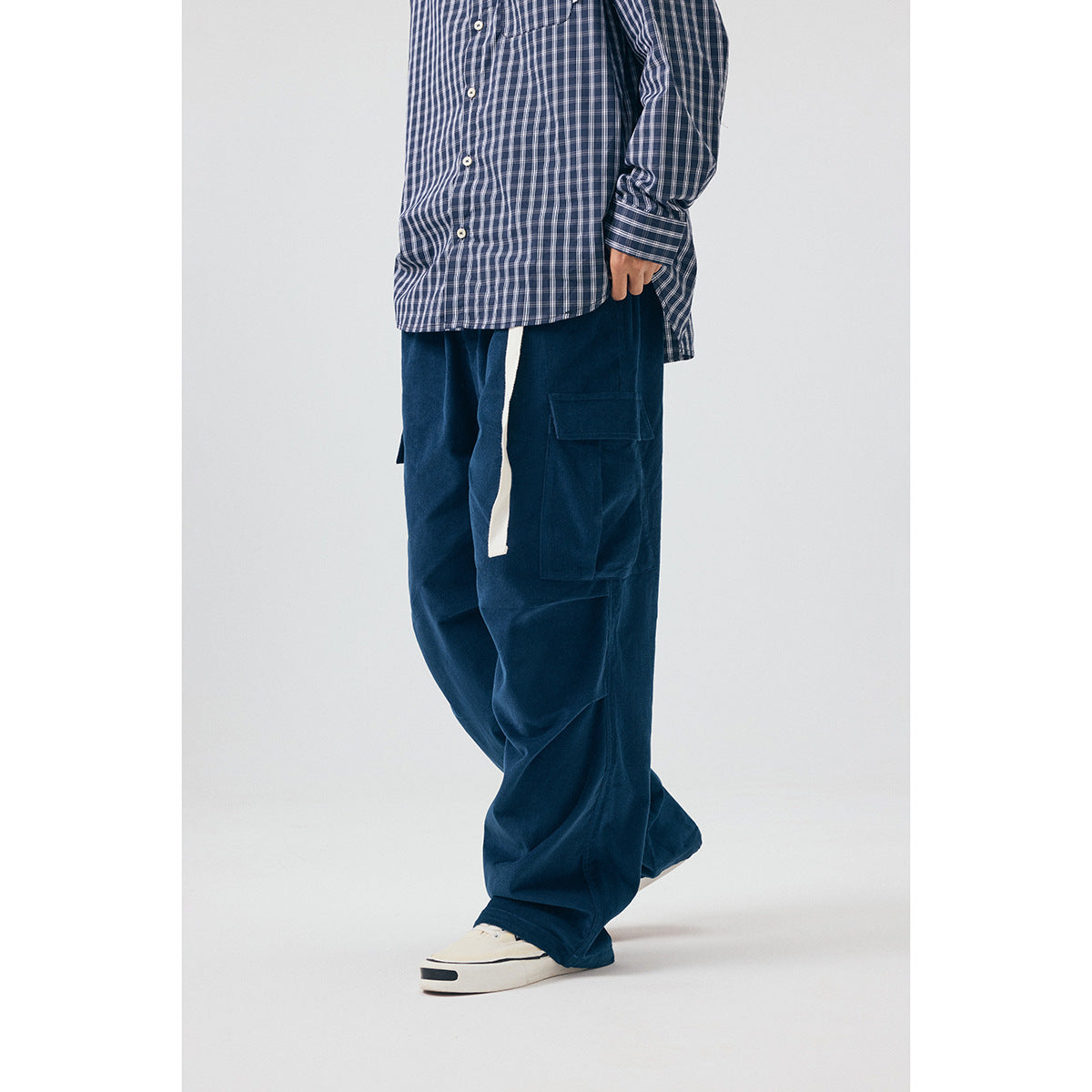 Side view of a model wearing loose navy cargo pants with a large thigh pocket and a long white drawstring.