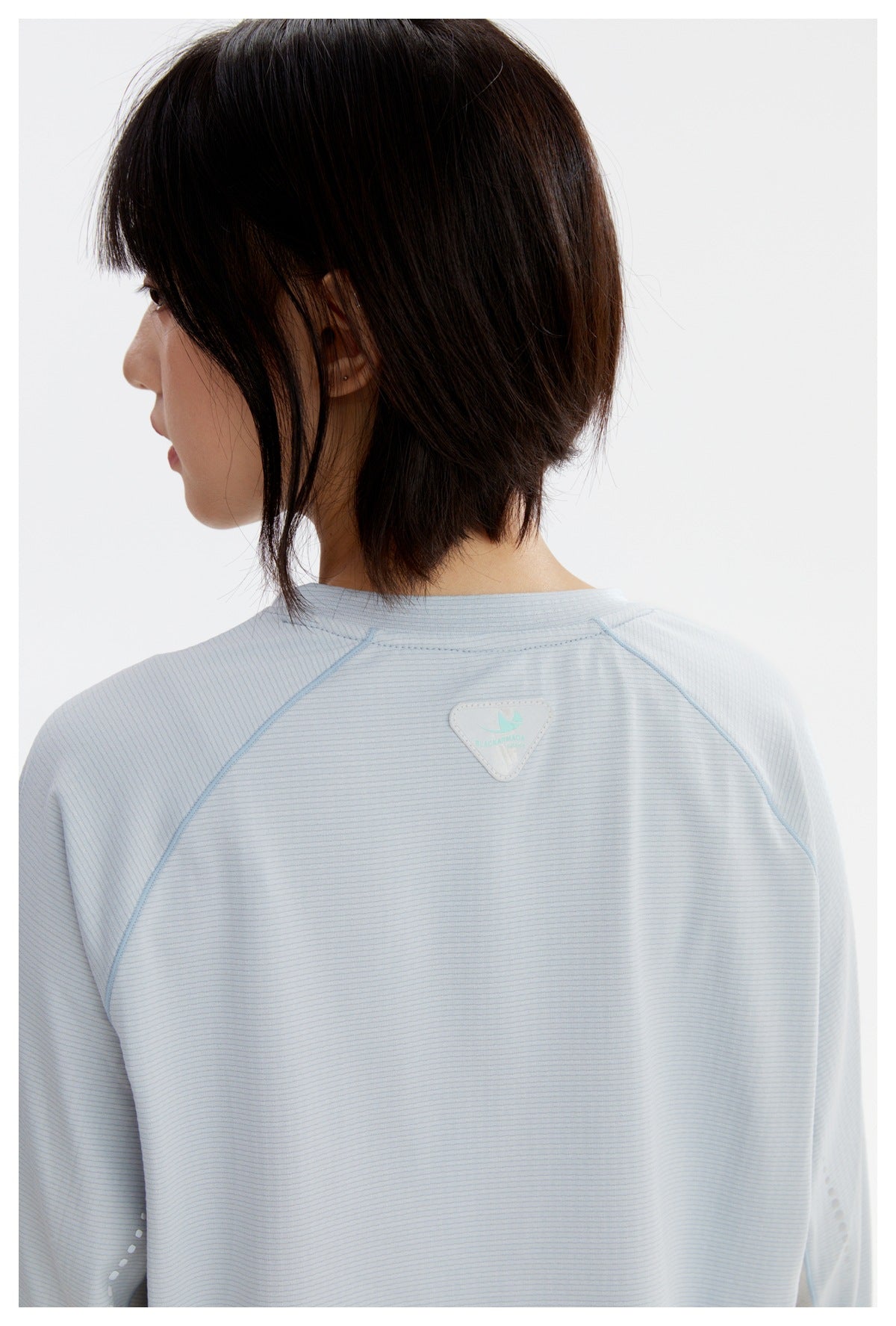 Close-up of the pale blue shirt's back neckline, raglan seams, and small triangular patch.