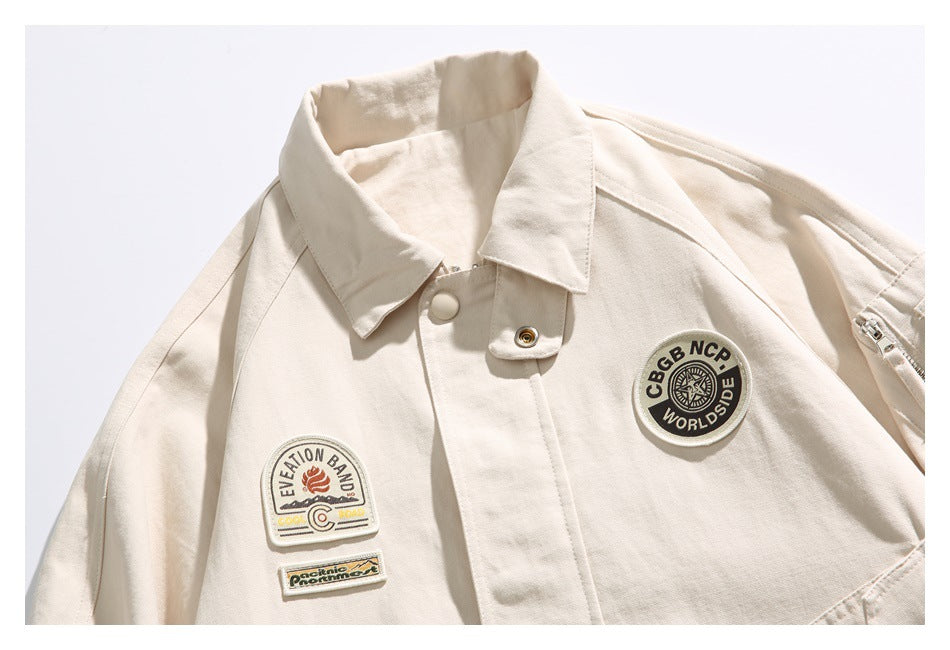 Close-up of an ivory jacket front with a pointed collar, snap-button placket, and several embroidered patches.