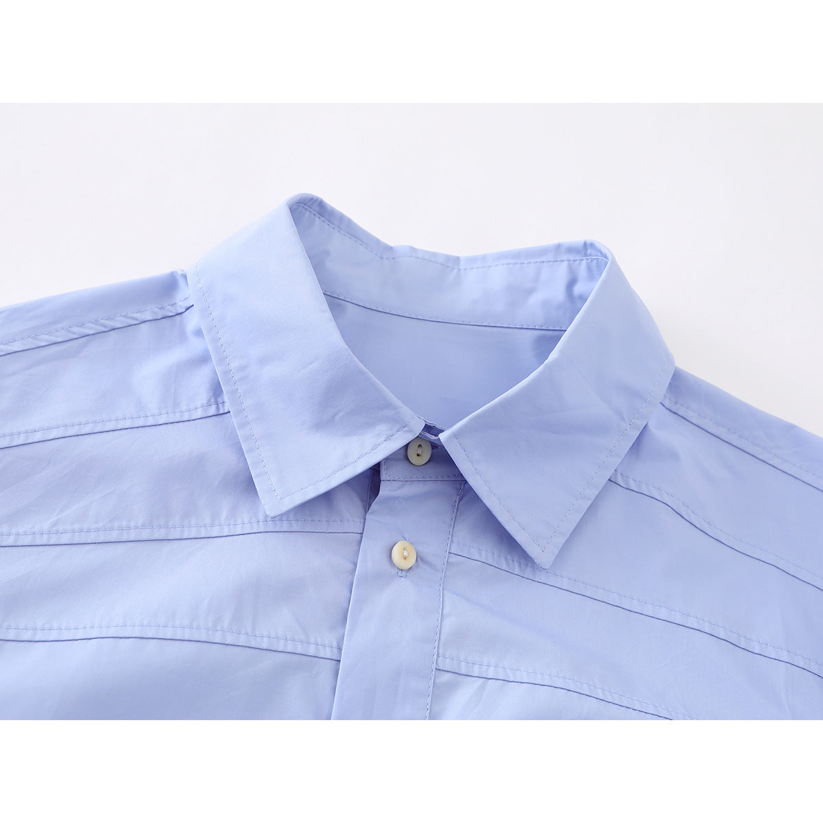 Close-up of a light blue button-up shirt collar, top buttons, and stitched shoulder panels.
