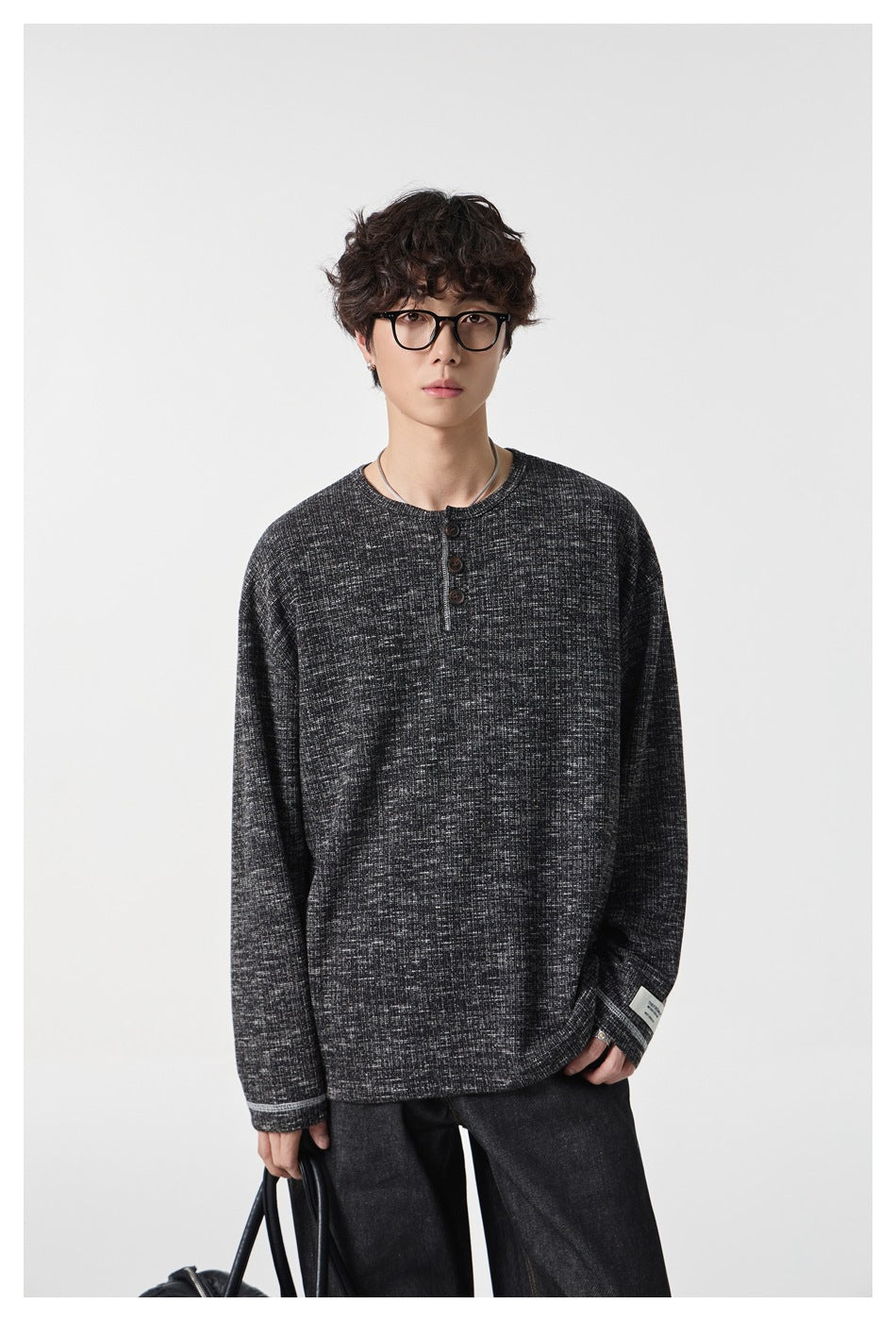 Model wearing a charcoal marled long-sleeve Henley with a three-button placket and dark wide-leg trousers.