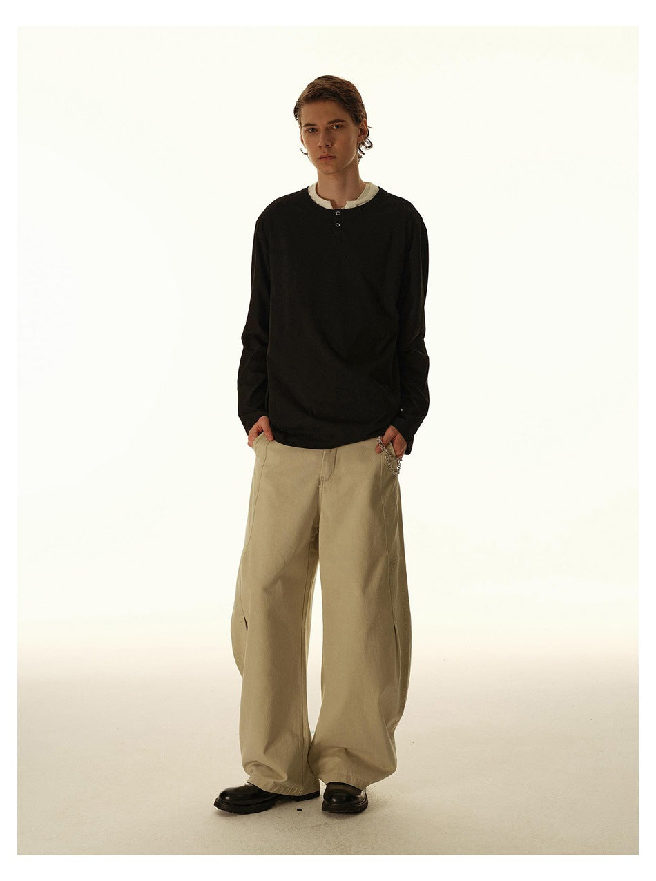 Model wearing a black long-sleeve henley with a white layer at the neckline and wide beige trousers.