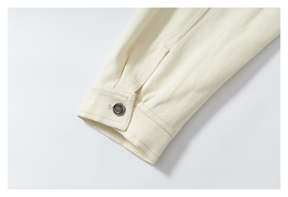 Close-up of an ivory sleeve cuff with a metal button, stitching, and a small embroidered mark.
