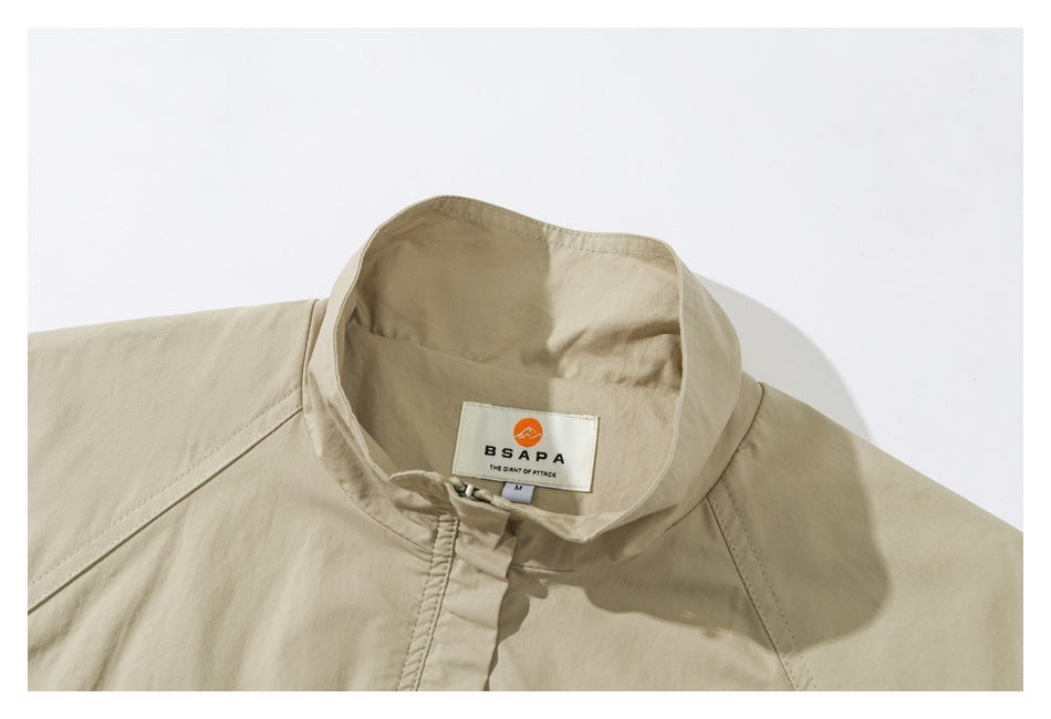 Close-up of a beige jacket's stand collar, covered front fastening, shoulder seams and sewn neck label.