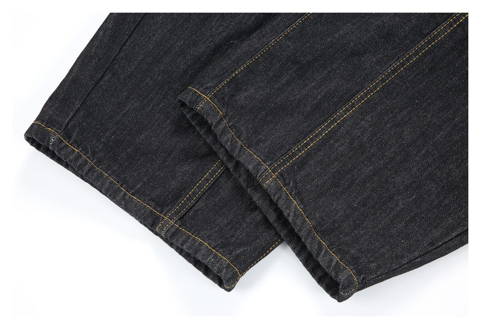 Close-up of two black denim leg hems with golden stitching.