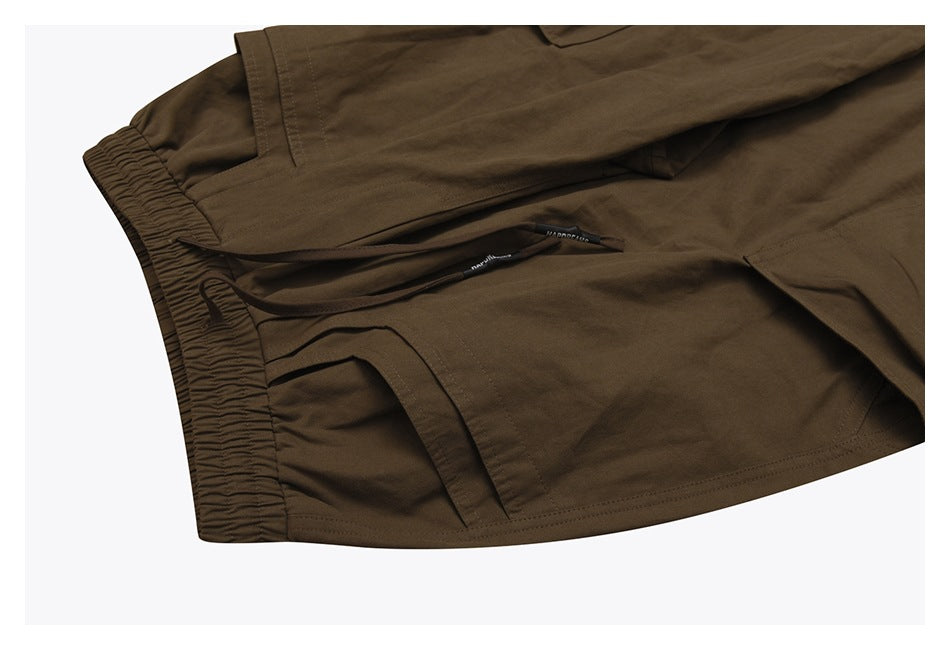 Close-up of olive-brown cargo pants showing the elastic waistband, drawstring and stitched pocket openings.