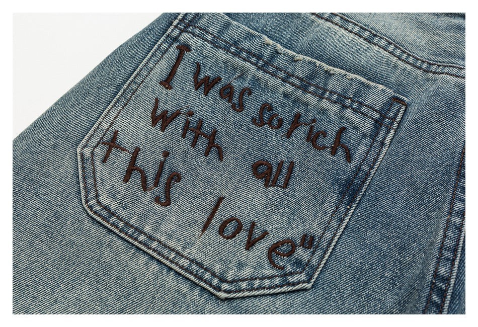 Close-up of a back pocket on blue jeans with a handwritten-style phrase stitched in dark thread.
