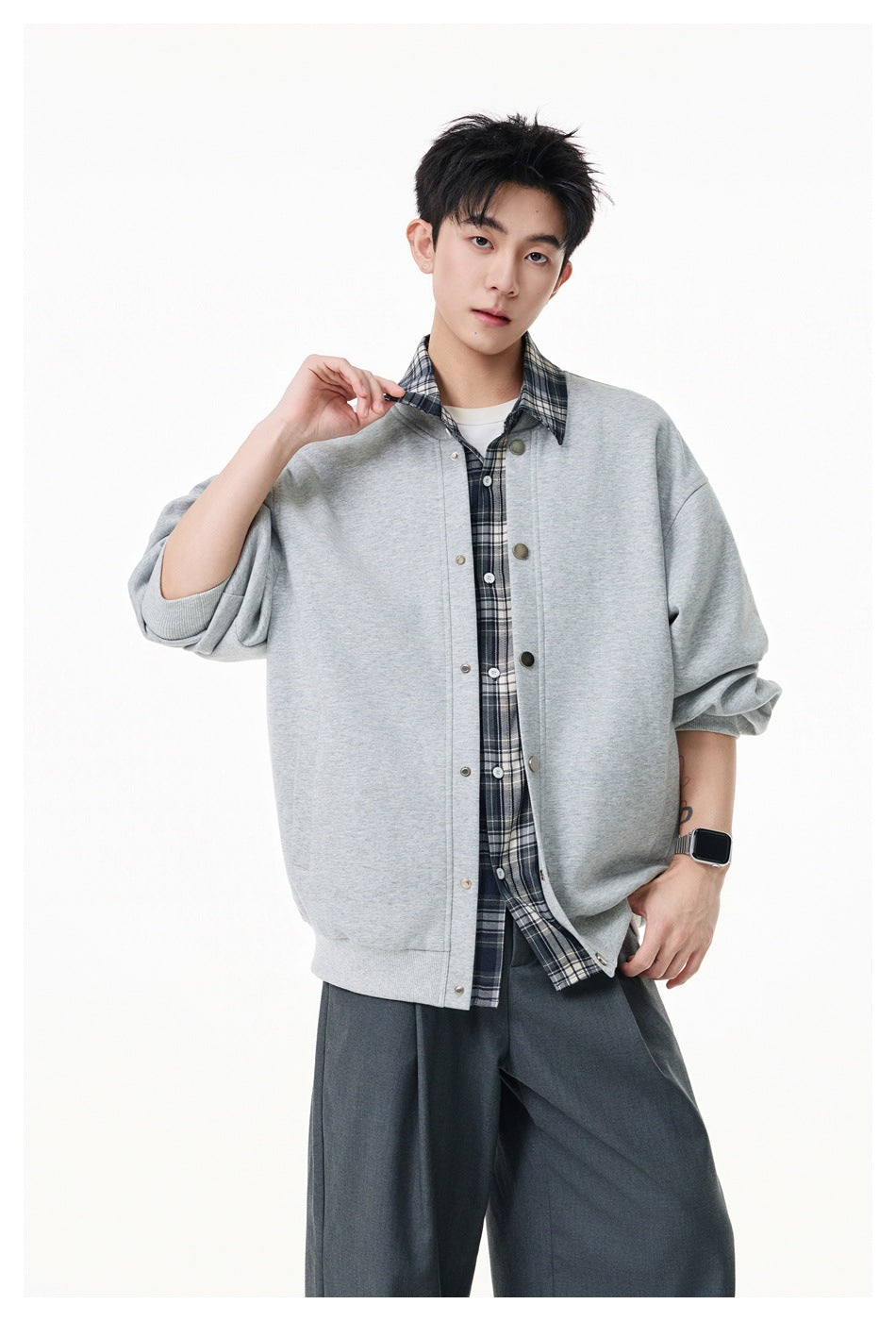Man wearing a heather gray snap-front jacket over a plaid shirt layer with gray pleated trousers