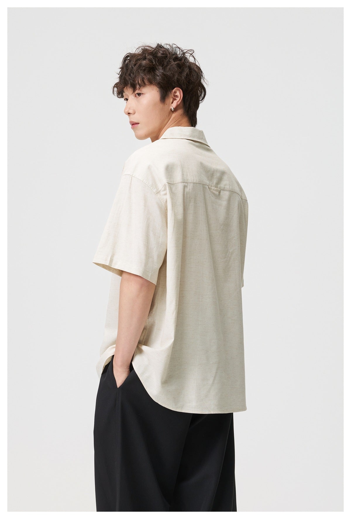 Male model showing the back of an off-white short-sleeve button-up shirt with a yoke seam.