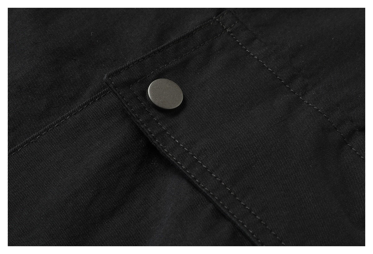 Close-up of a round snap fastener securing a stitched flap on black pants.