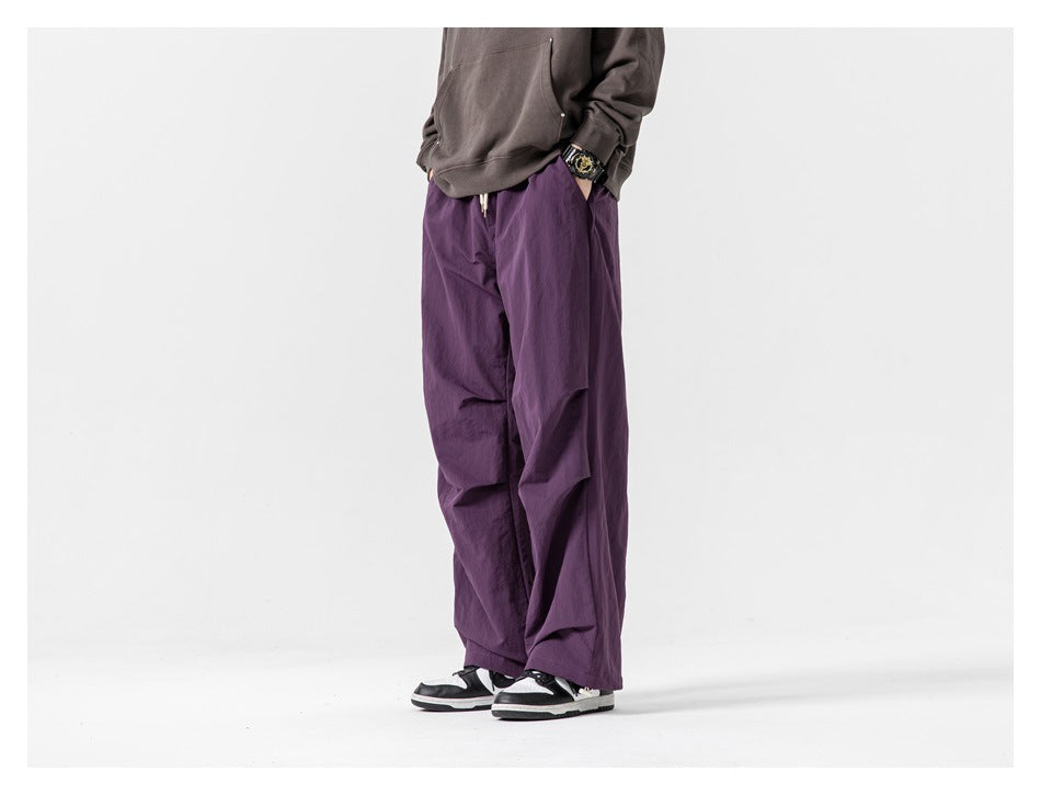 Cropped model wearing loose purple pants from a front three-quarter angle with black-and-white sneakers.