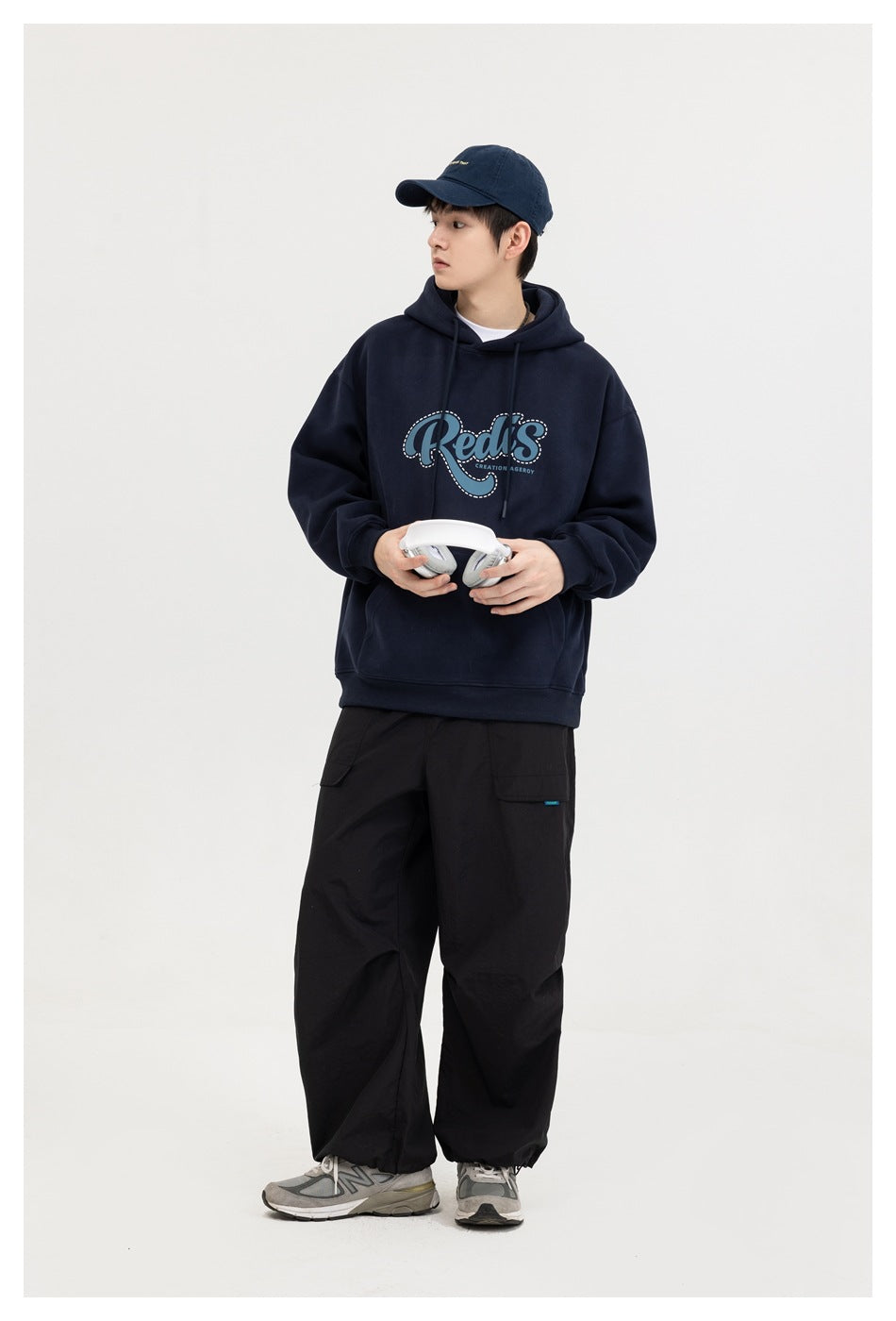 Model wearing a navy graphic hoodie with a kangaroo pocket, shown from the front with headphones in hand.