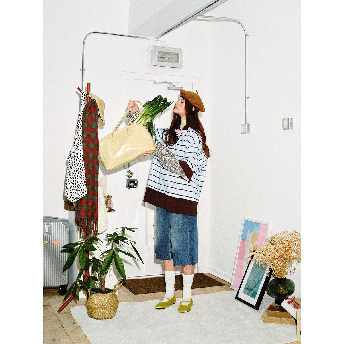 Model in a light blue striped top with brown trim and plaid sleeves, holding a yellow bag with greens.