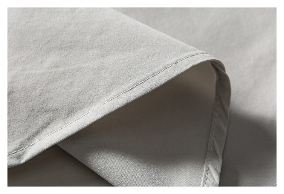 Close-up of a neatly stitched hem on light gray-white shirt fabric.