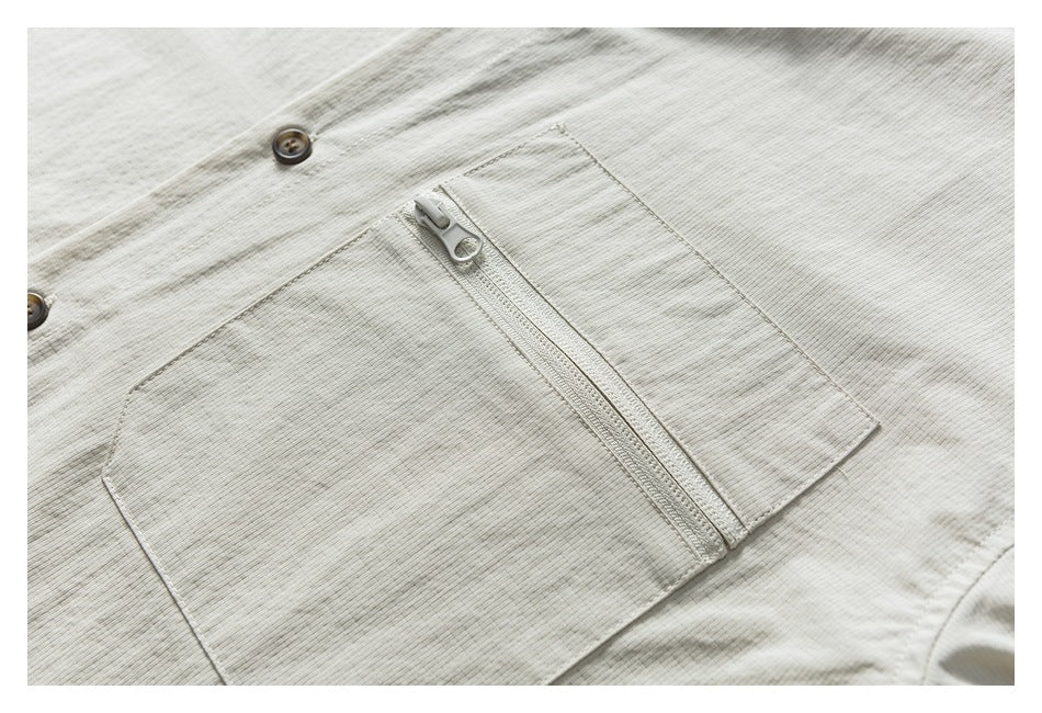 Close-up of an off-white shirt's chest pocket with a vertical zipper and nearby buttons.