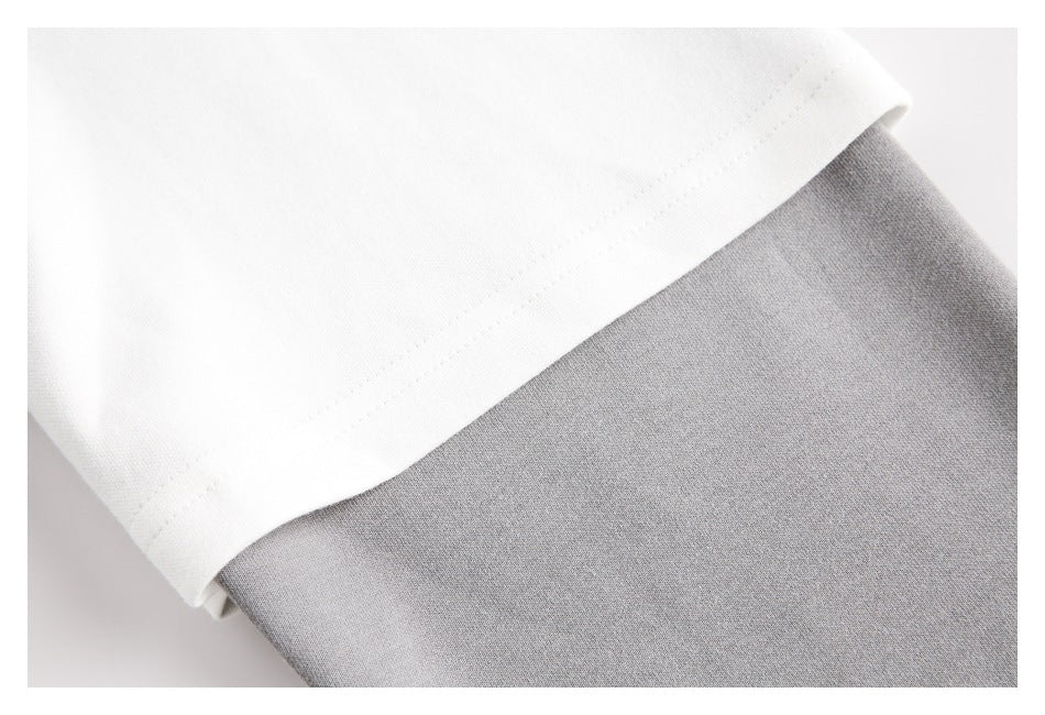 Close-up of a white garment hem overlapping gray fabric, showing the hem stitching.