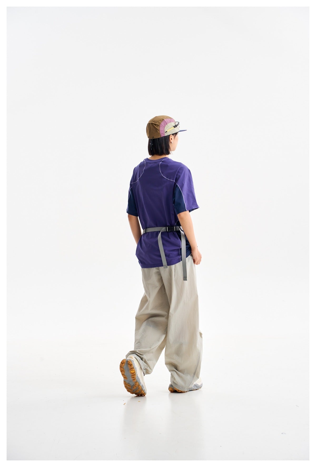 Rear view of a model wearing a purple short-sleeve T-shirt with contrasting dark sleeves and curved seam details.