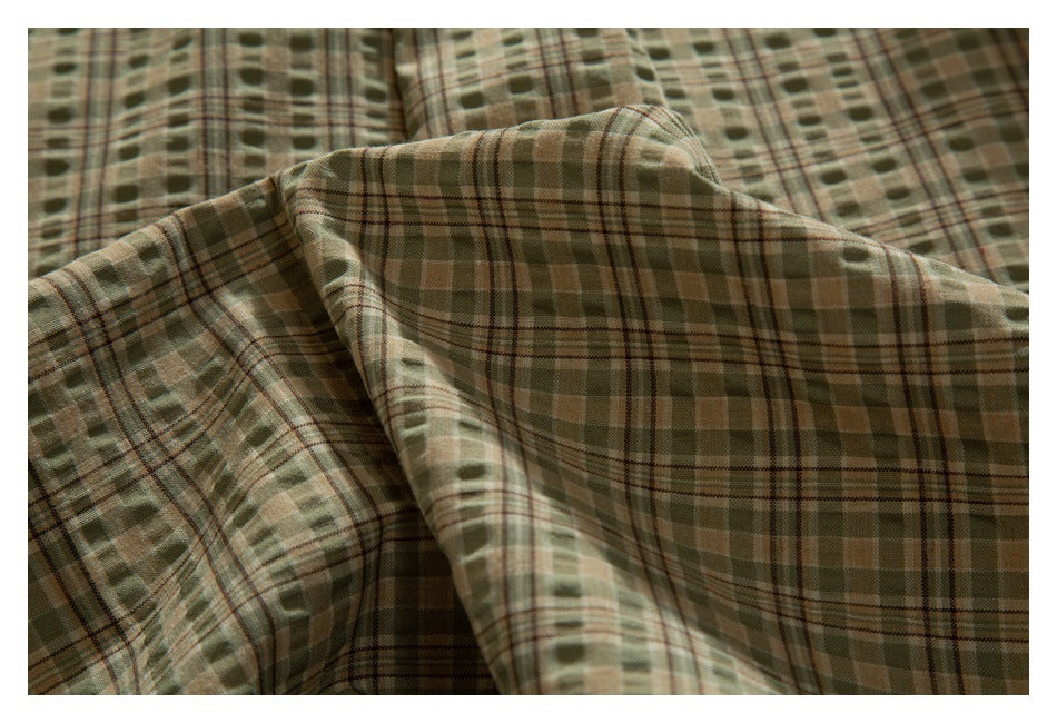 Close-up of draped olive, tan, and brown plaid fabric showing its patterned surface.