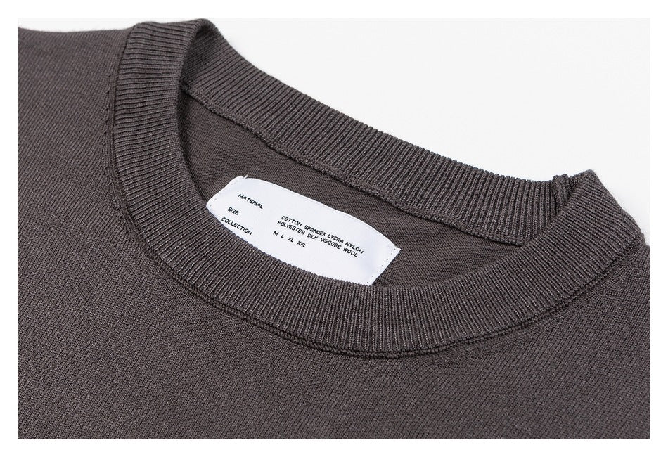 Close-up of a charcoal gray knit sweater's ribbed crew neckline and inner label.