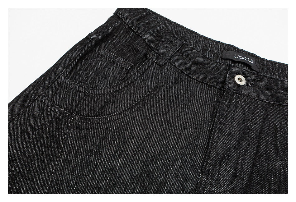 Close-up of black trousers showing a curved front pocket, waistband and metal button.