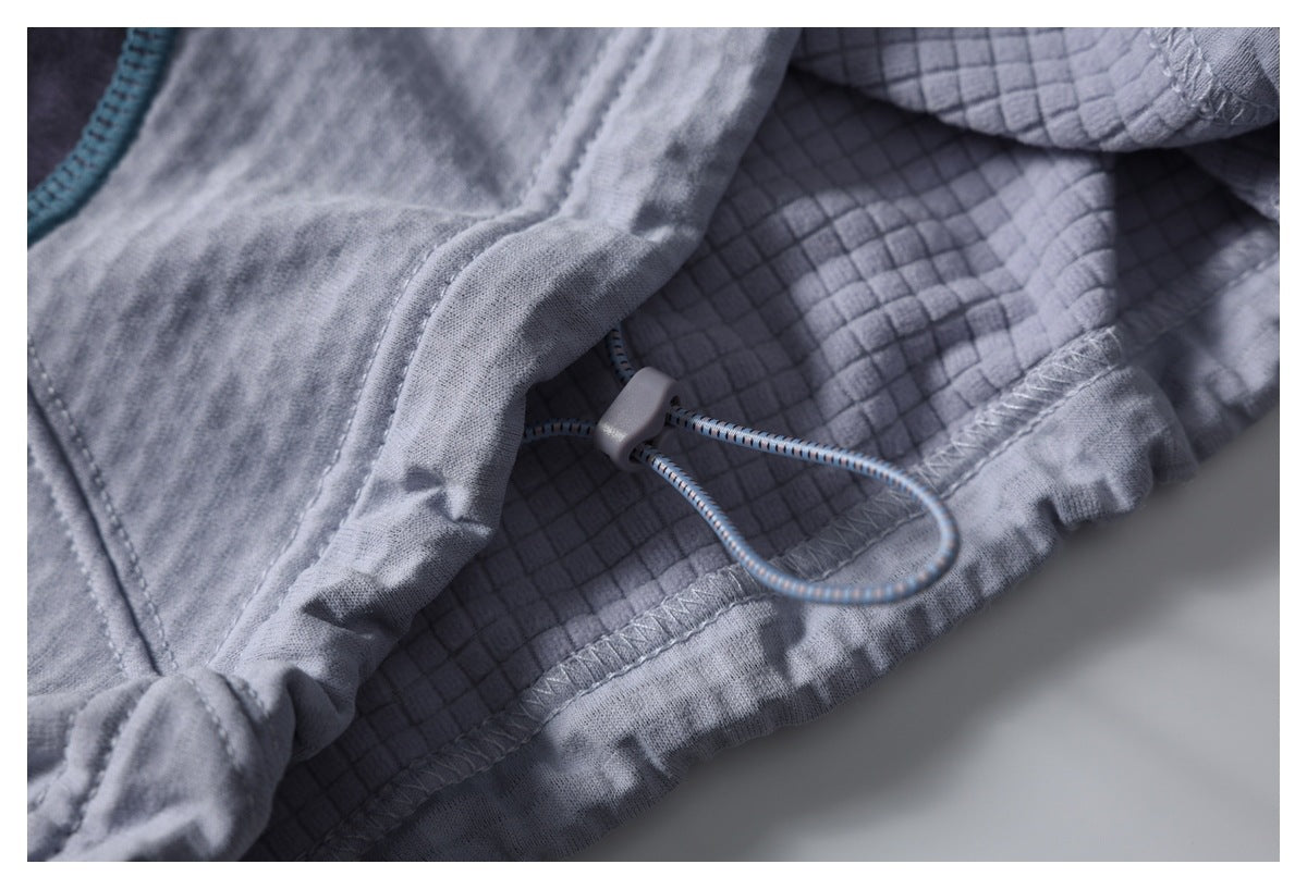 Close-up of gray garment construction with a small cord loop and toggle beside textured lining and stitched seams.