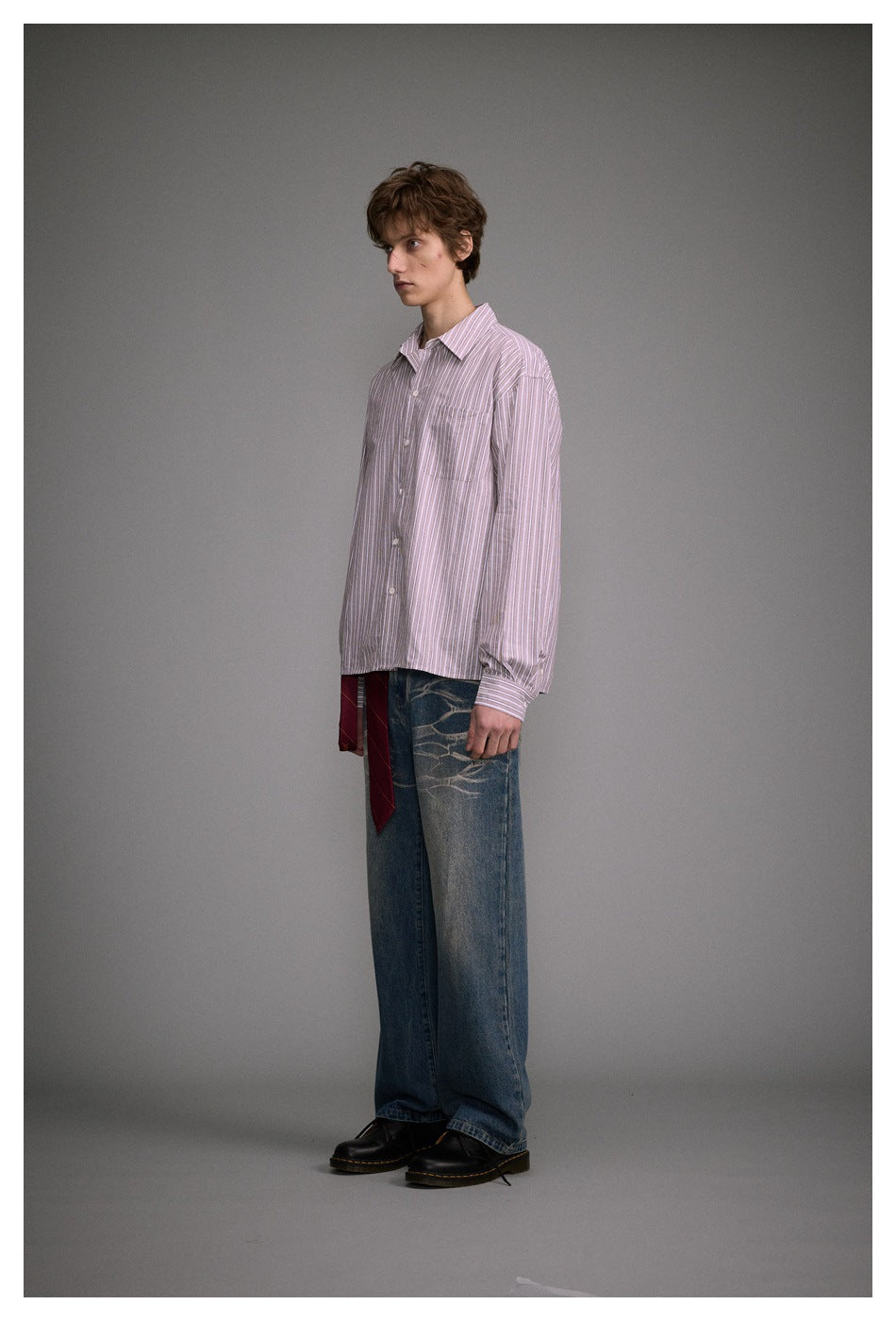 Three-quarter view of a model wearing a pink-and-white striped button-up shirt and loose blue jeans.