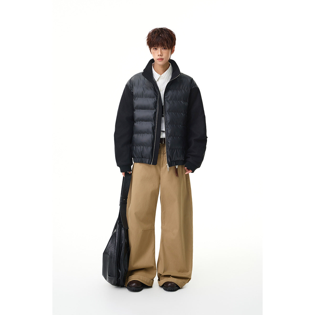 Model wearing a black quilted zip jacket with dark sleeves, styled with loose tan trousers.