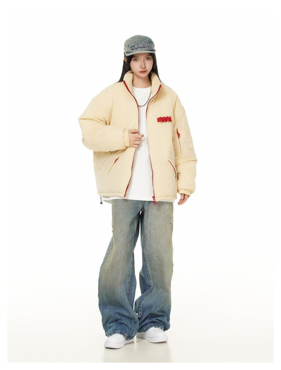Full-length model wearing an open cream padded jacket with red trim, wide jeans, and a denim cap.
