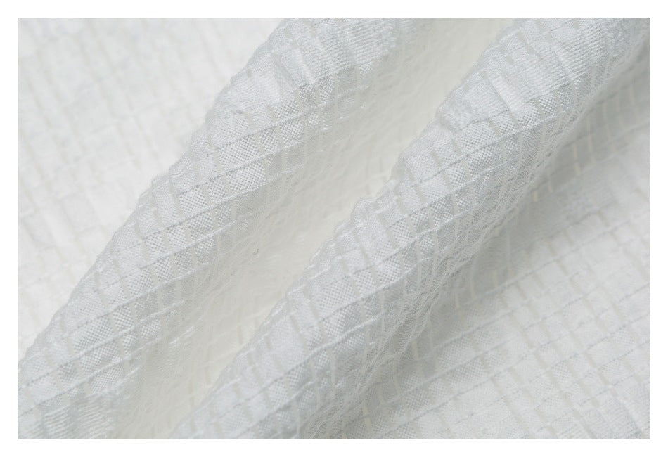 Macro view of the white shirt's raised geometric weave and folded fabric edge.