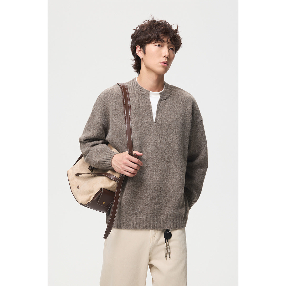 Model wearing a taupe split-neck sweater with ribbed cuffs and hem, paired with cream trousers.