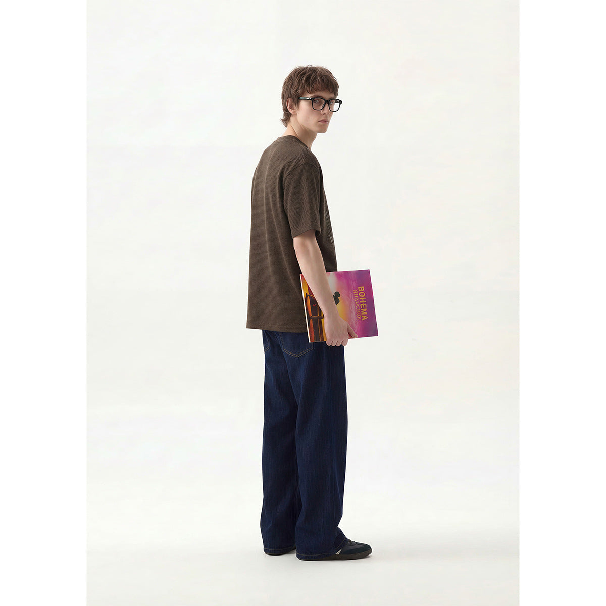 Model in a dark brown T-shirt and wide-leg jeans, turned to show the shirt's plain back.