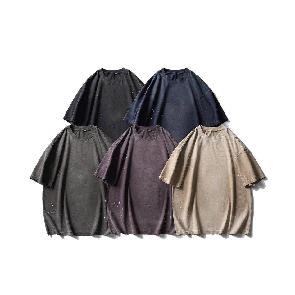 Five oversized crew-neck T-shirts in black, navy, charcoal, muted plum, and beige, with scattered distressed flecks.