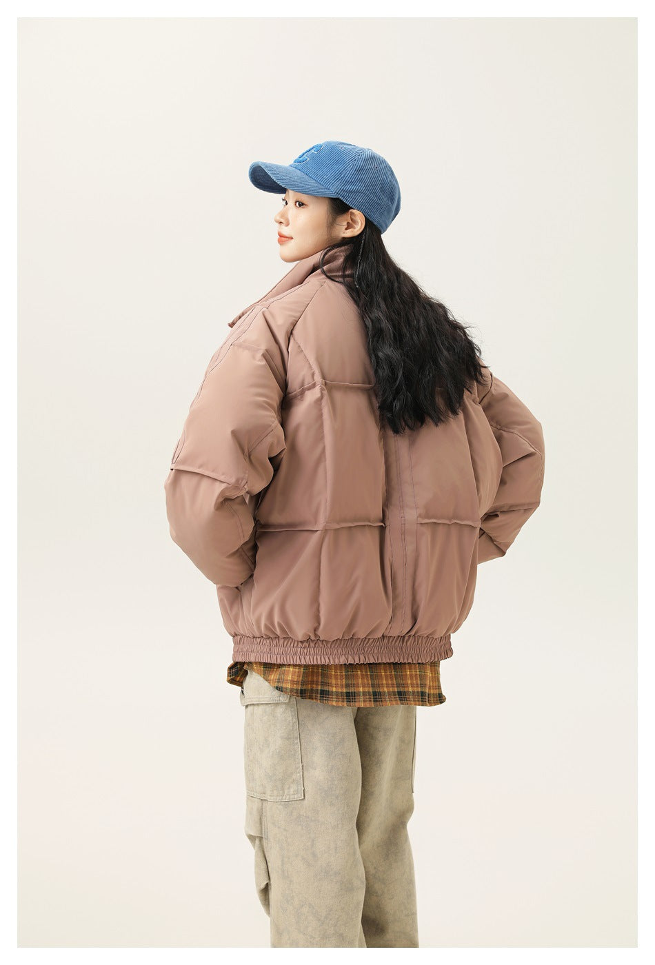 Model wearing a dusty pink puffer jacket over a plaid shirt, side and back view showing quilted panels and elastic hem