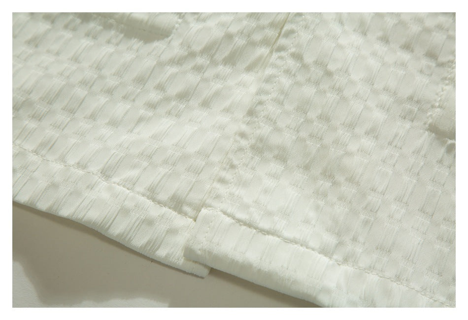 Close-up of the stitched hem and textured weave of an ivory shirt.