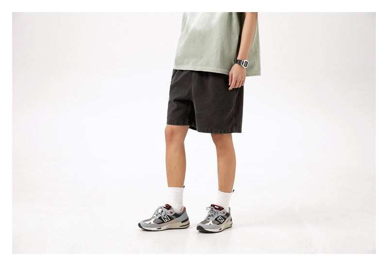 Model wearing charcoal shorts, shown from a front-side angle against a plain white studio background.