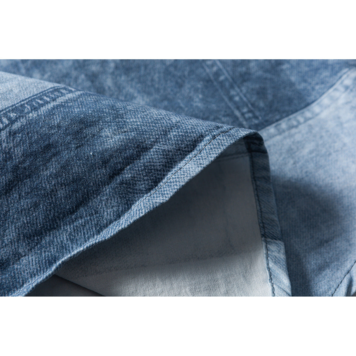 Close-up of a turned edge and stitching on blue washed shirt fabric.