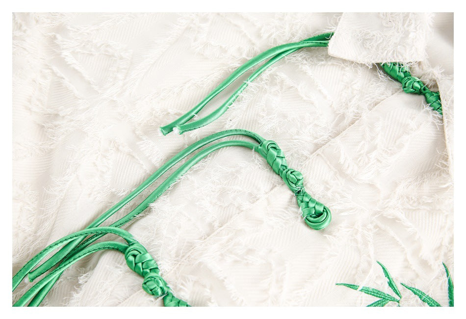 Close-up of braided green tie closures against the ivory shirt's fringed geometric fabric.