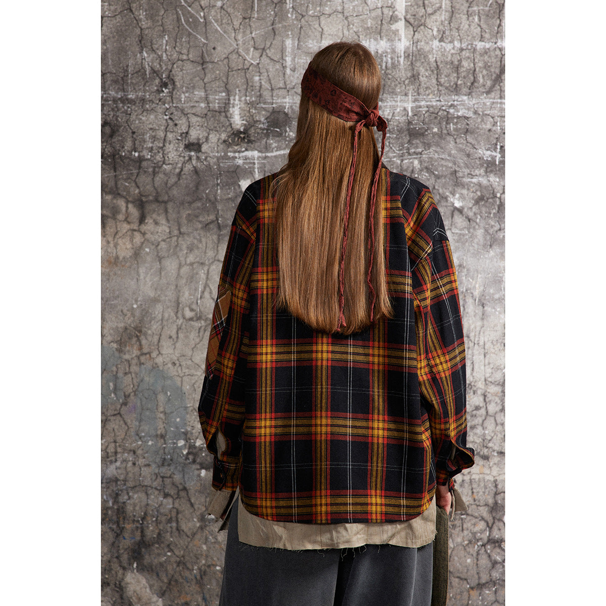 Back view of a model in an oversized black plaid shirt-jacket with red and mustard stripes.