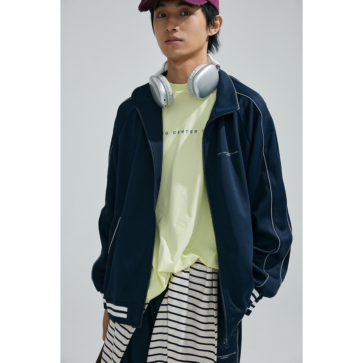 Model wearing a navy zip jacket with white piping over a pale yellow tee and striped shirt, shown from the front.