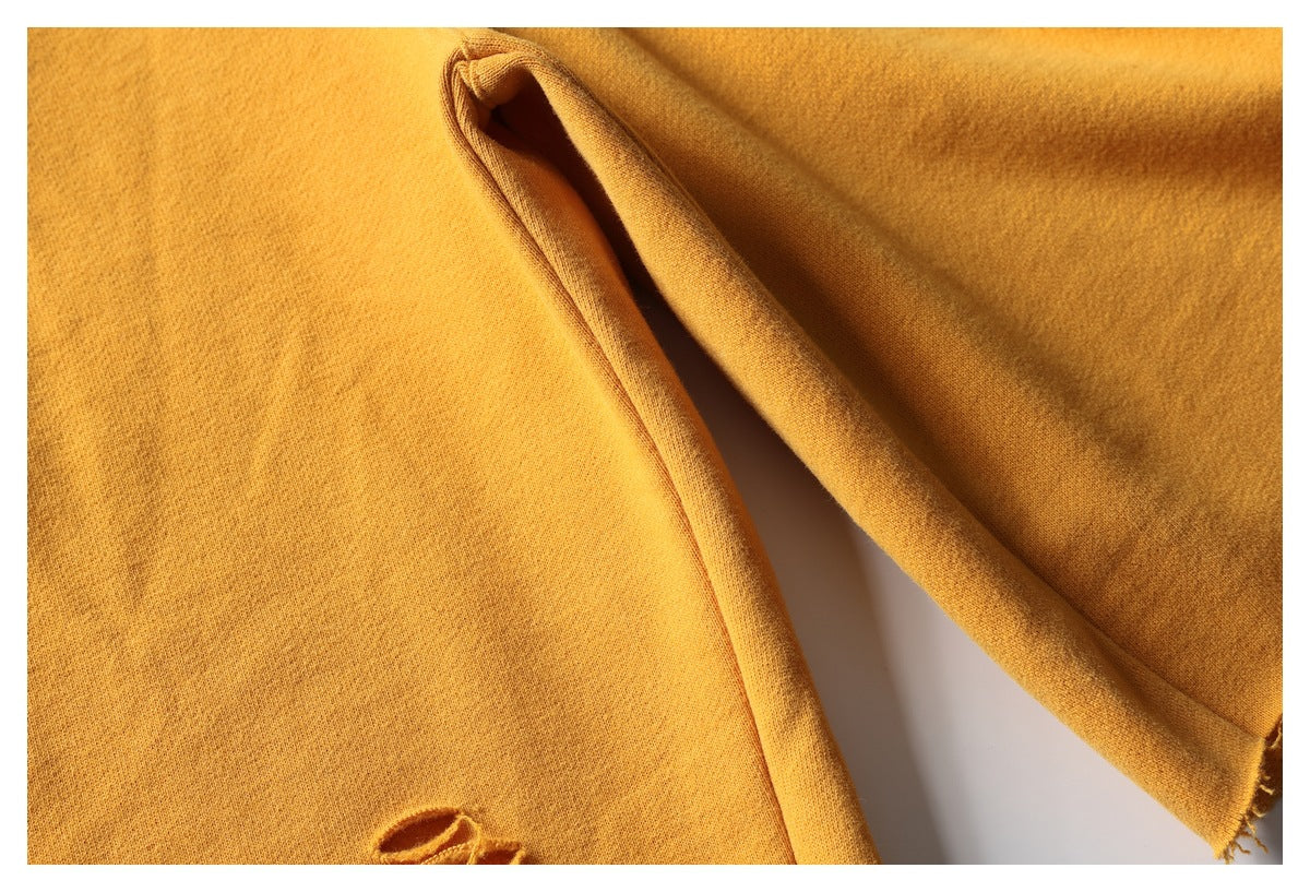 Close-up of mustard garment fabric and a folded seam, with part of a distressed stitched motif visible.