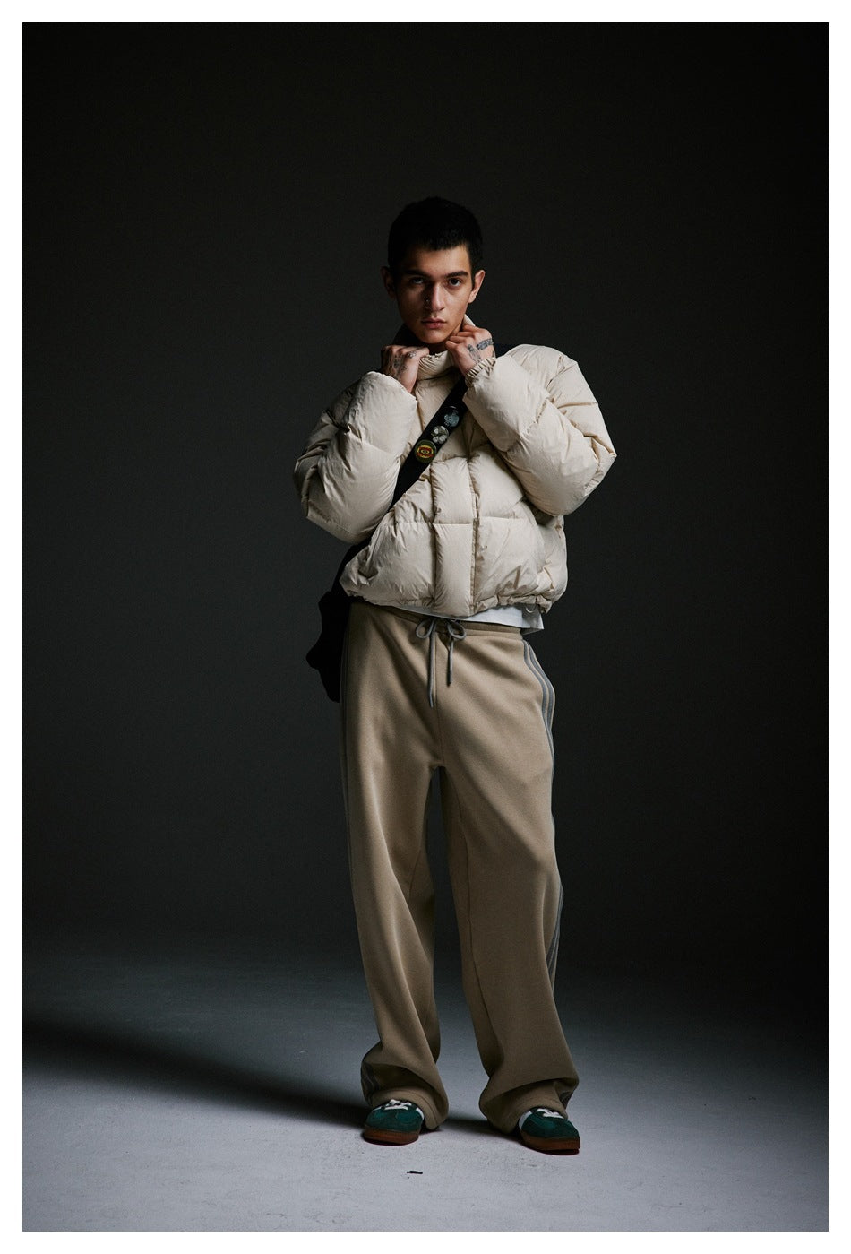 Model adjusting the collar of a cream puffer jacket, paired with loose taupe pants.