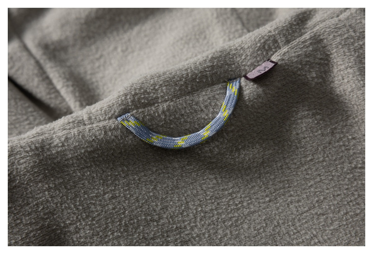 Close-up of gray fleece fabric and a curved blue-and-yellow cord detail beside a small tab.