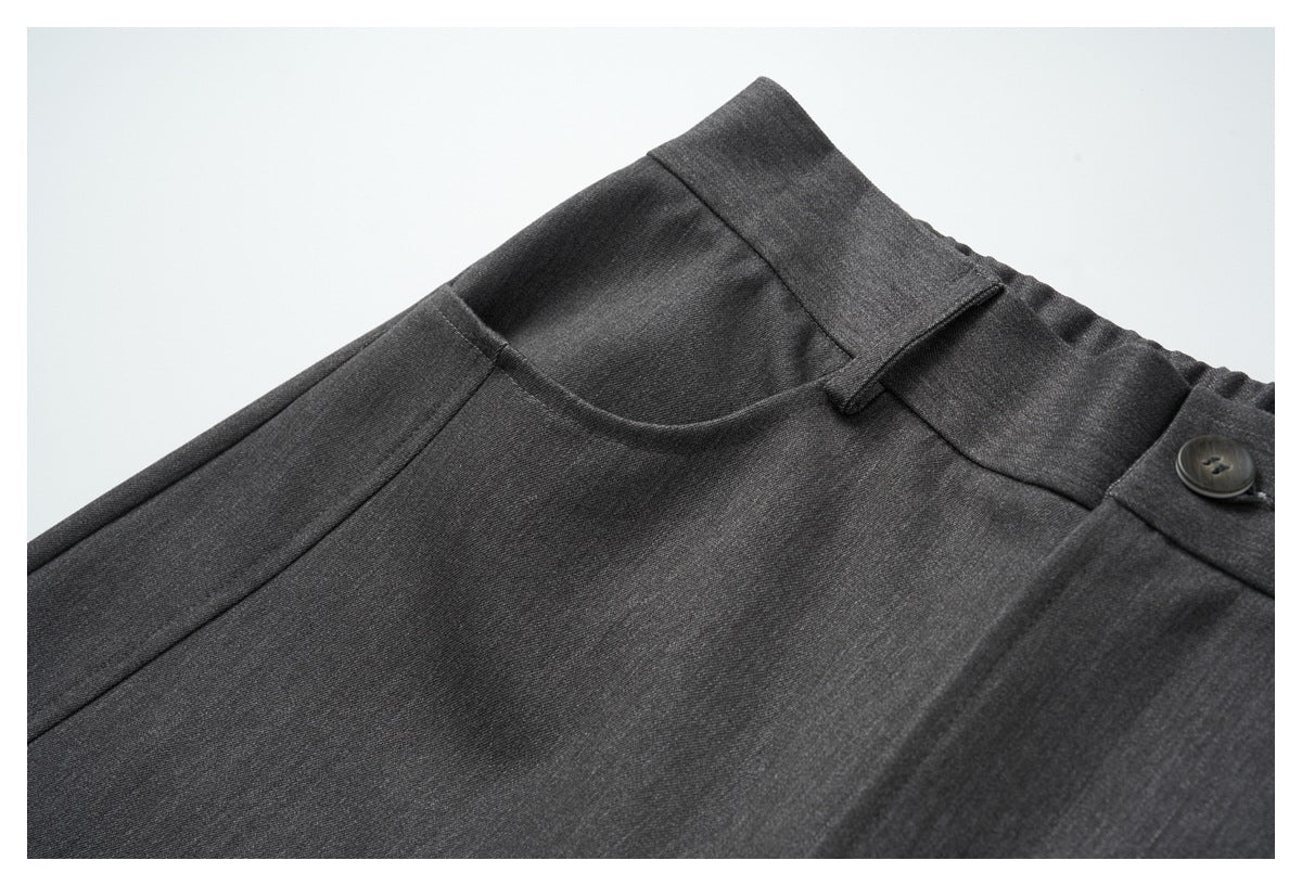 Close-up of the charcoal gray trousers' waistband, belt loop, button, and curved front pocket.